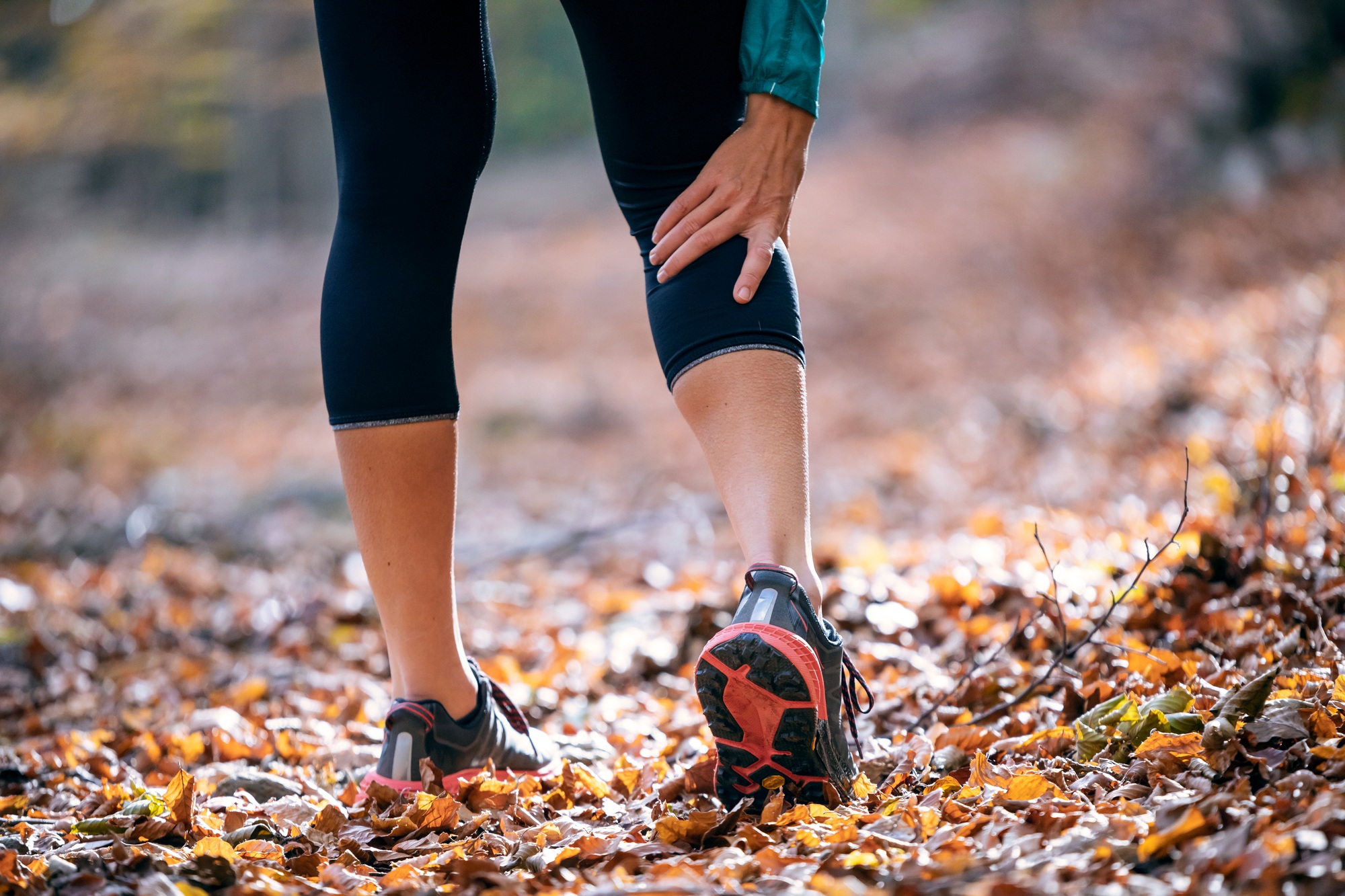 Sporty woman has muscle injury and holding her painful leg in the forest.
